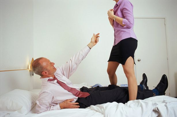 Woman-standing-over-businessman-on-bed
