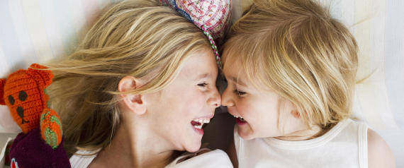 Portrait of two young sisters lying face to face in bed