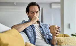 young man coughing while drinking tea in the livin 265x160