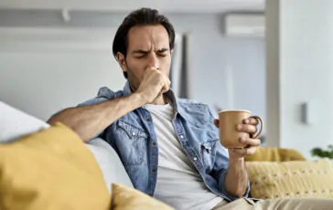 young man coughing while drinking tea in the livin 364x230
