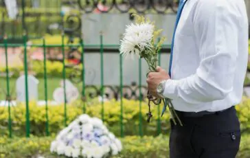 Funerale, uomo che porta i fiori alla tomba