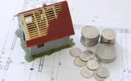 Miniatura casa in costruzione su progetto, monete a fianco.