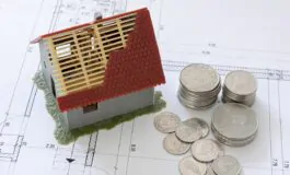 Miniatura casa in costruzione su progetto, monete a fianco.