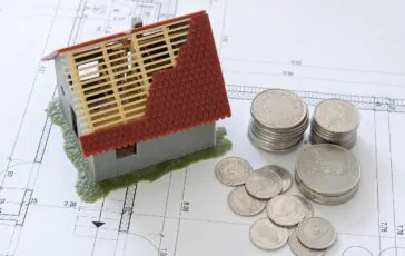 Miniatura casa in costruzione su progetto, monete a fianco.