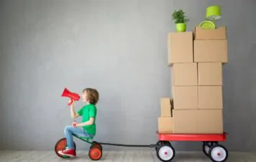 caricatura del trasloco con il bambino che trasporta i pacchi con il triciclo 364x230